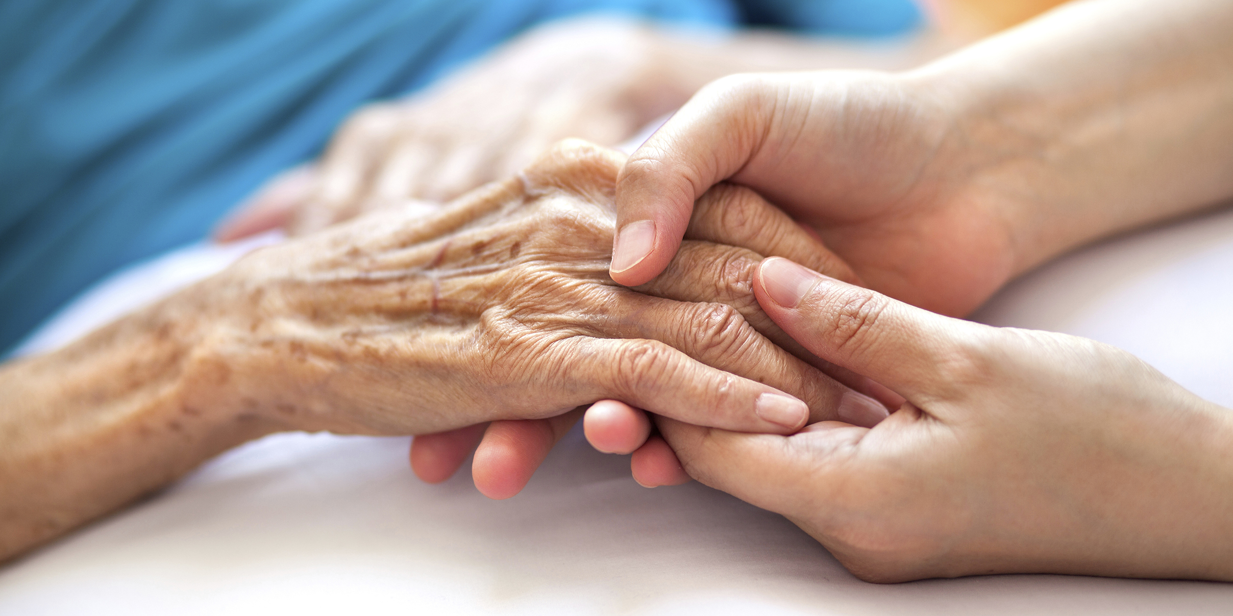 close-up of a person holding hands with an elderly relative who is lying in a bed
